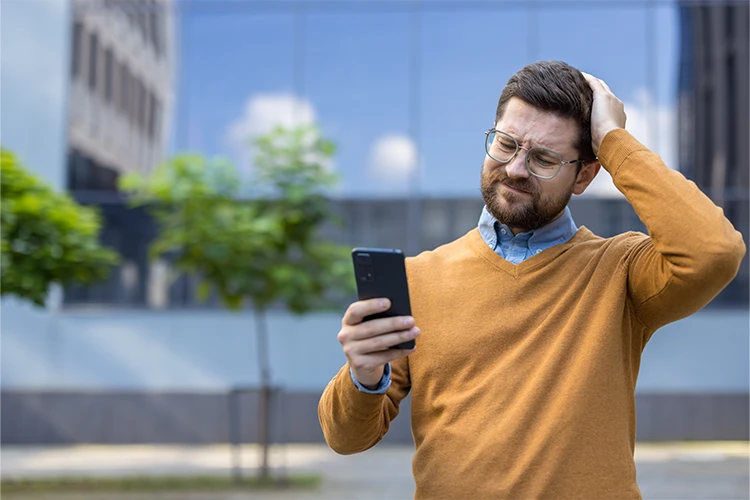 homme dehors regardant son téléphone avec une main posée sur la tête
