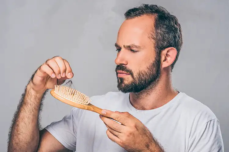 Homme observant des cheveux tombés dans sa brosse après le coiffage.