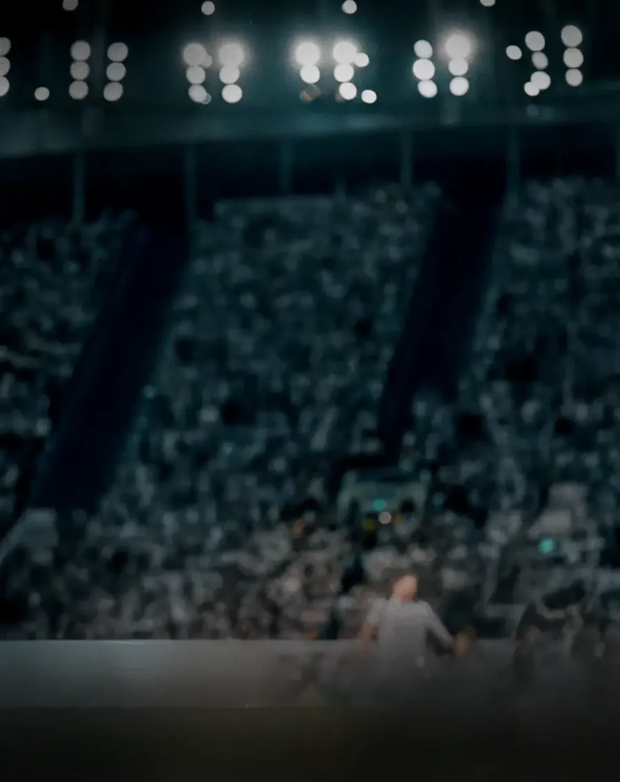 Vue floue d’un stade de football bondé la nuit, avec des projecteurs brillants et des tribunes pleines